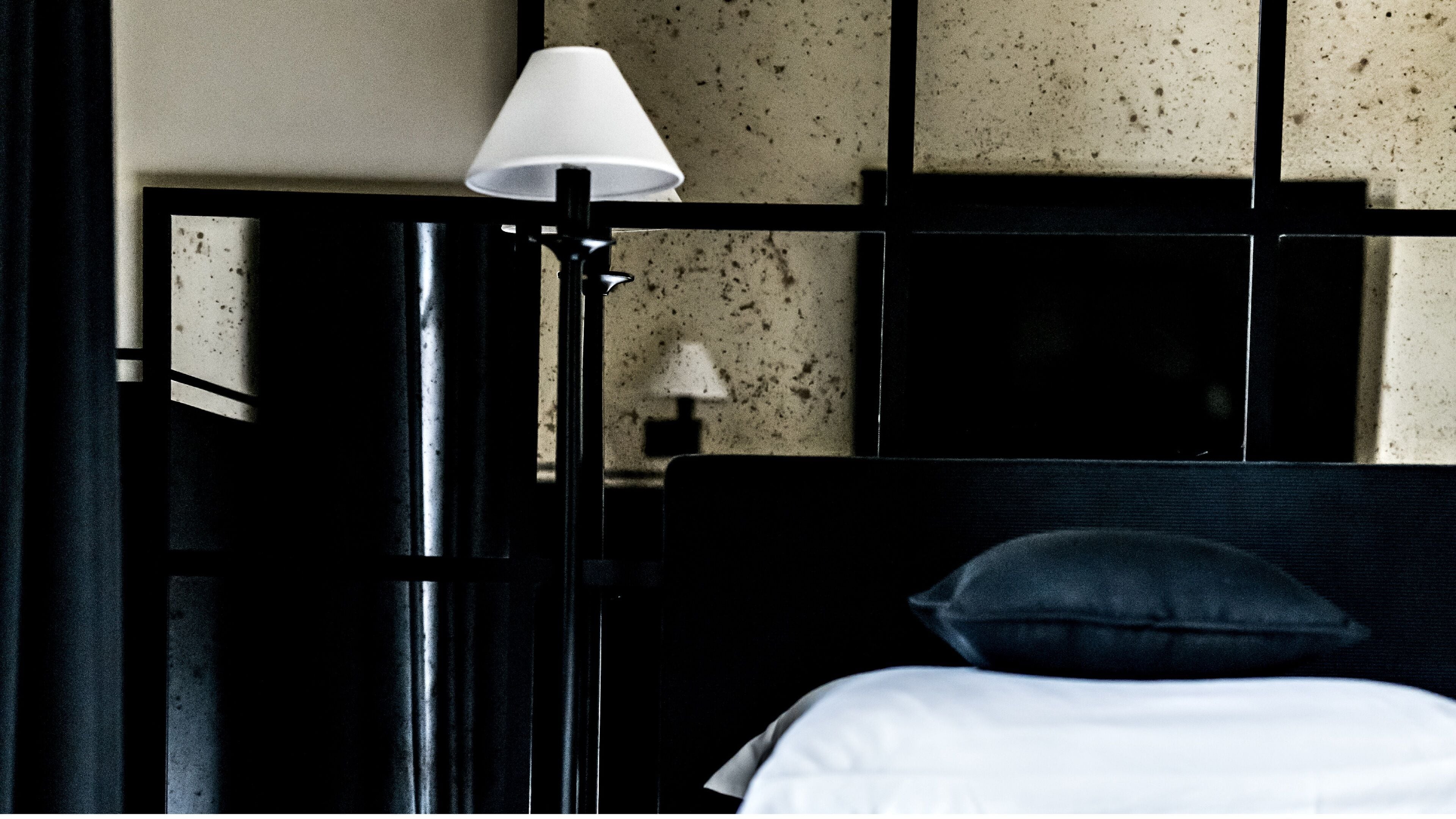 A hotel room with a black headboard, a white bedspread, and a lamp on a bedside table.