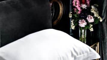 Een wit kussen op een donkere bank, een vaas met bloemen en een spiegel met gouden lijst.