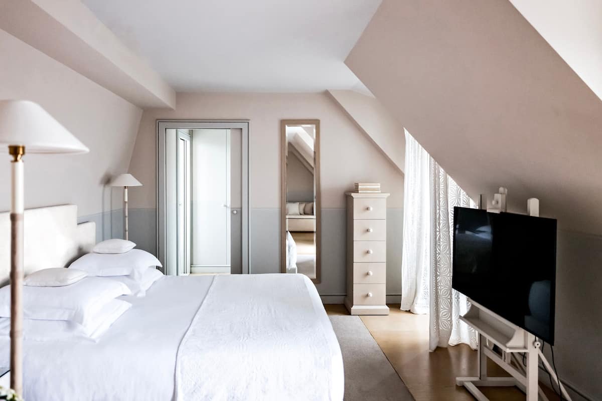 A modern hotel room with a large bed, a TV, a wardrobe, and a mirror.