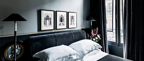 Un lit bien fait, avec du linge de lit blanc, une tête de lit sombre et un plan architectural encadré accroché au mur.