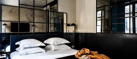 Habitación de hotel moderna con una cama grande, varios espejos y vistas de la ciudad a través de amplias ventanas.