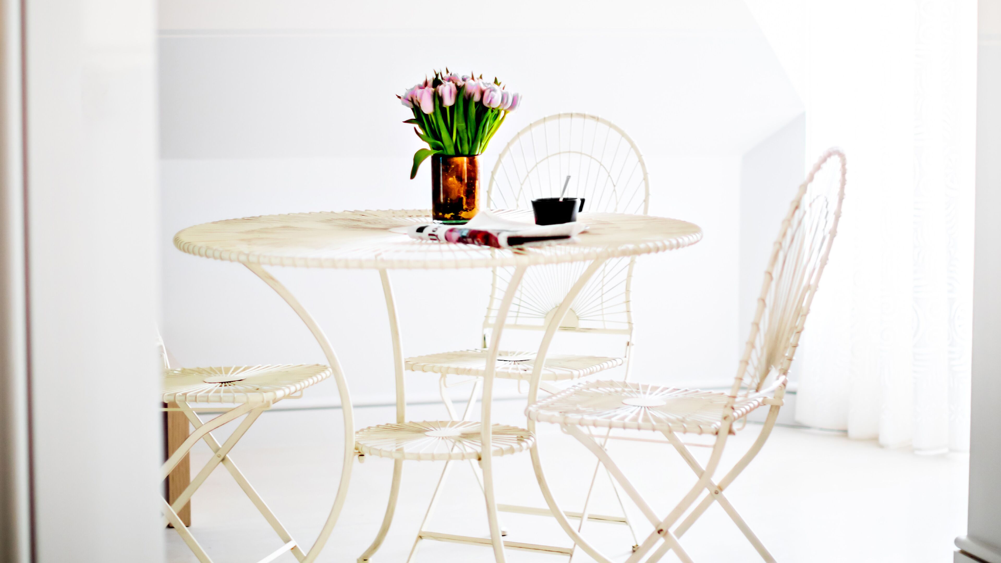 Una mesa redonda blanca de mimbre con un florero y una taza negra encima.