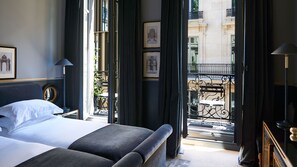 Ein Hotelzimmer mit einem großen Bett, einem Nachttisch, einem Spiegel und Blick auf die Stadt durch geöffnete Vorhänge.