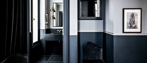 A modern bathroom with a dark color scheme, a large mirror, and a framed artwork on the wall.