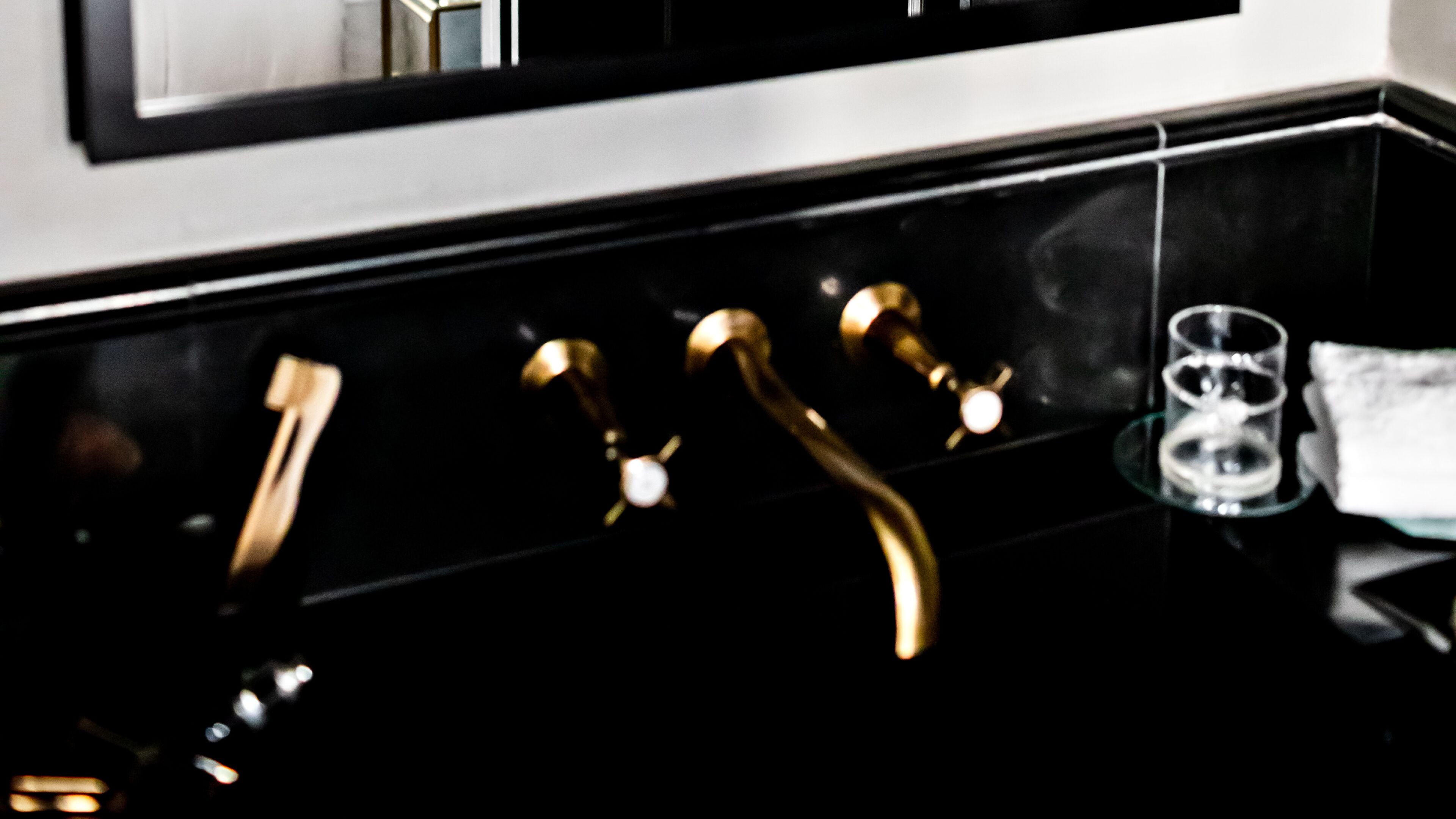Un lavabo de salle de bain noir et doré, avec un miroir au-dessus.