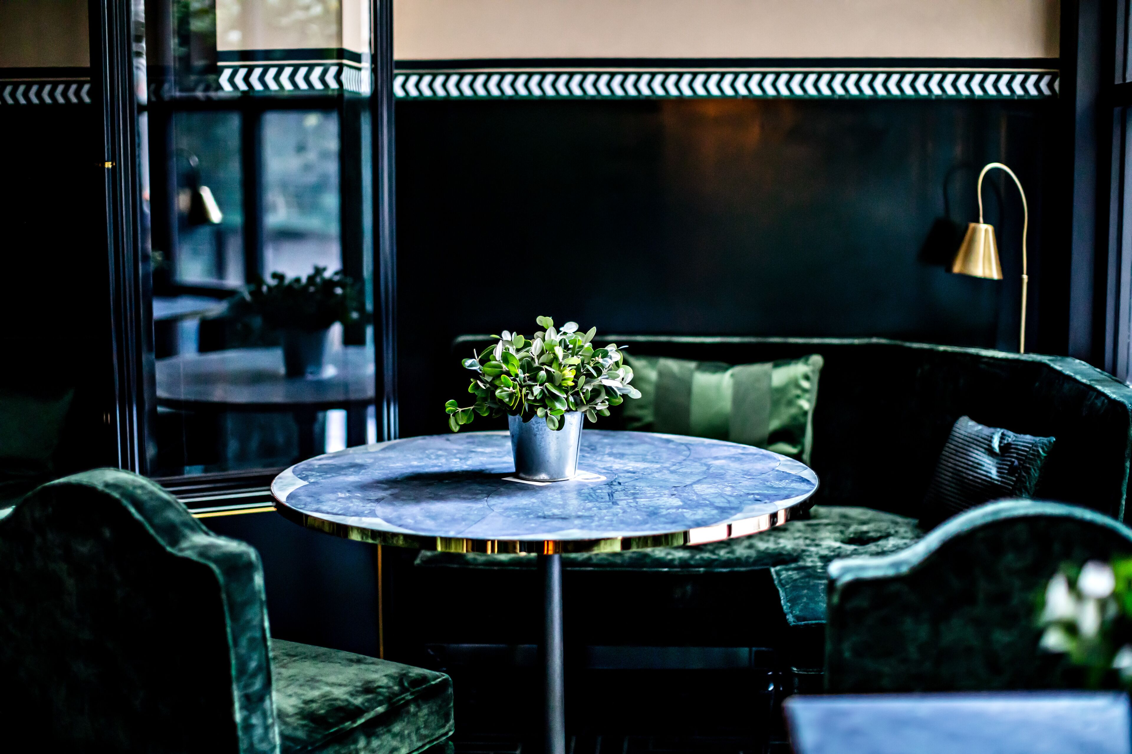 A round table with a potted plant, green upholstered seating, and a wall-mounted lamp.