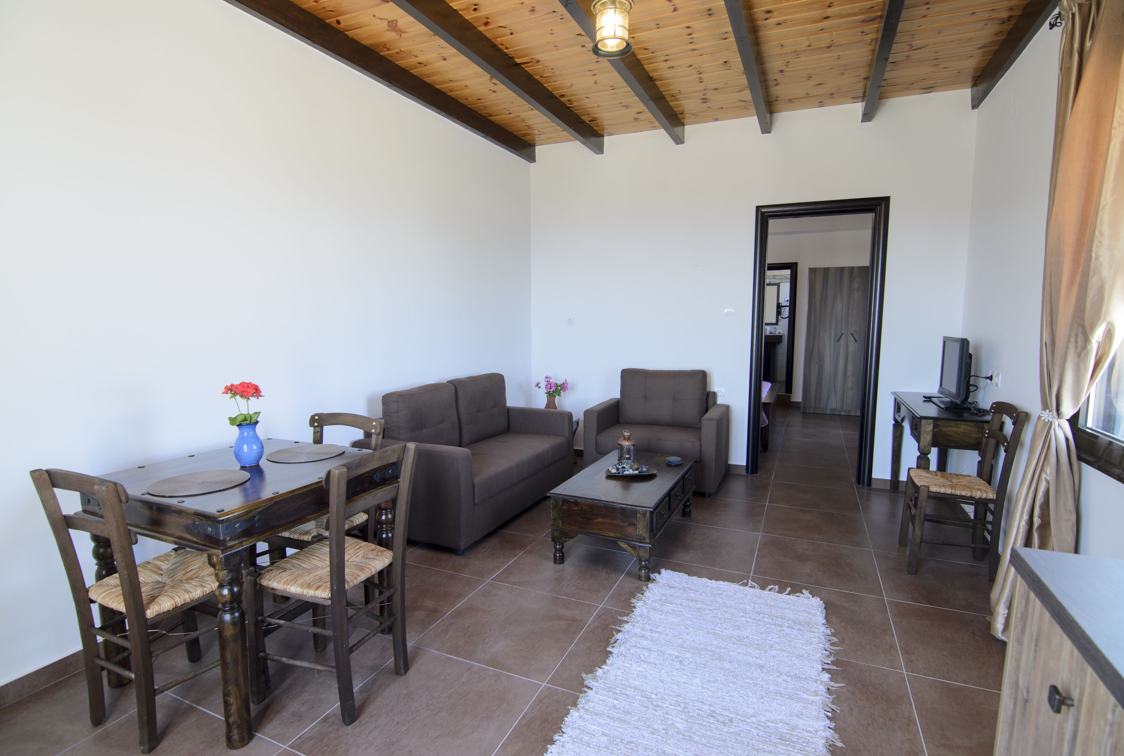A living room with a wooden ceiling, a dining table with chairs, a sofa, a coffee table, and a TV.