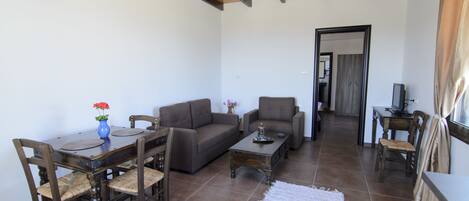 A living room with a wooden ceiling, a dining table with chairs, a sofa, a coffee table, and a TV.