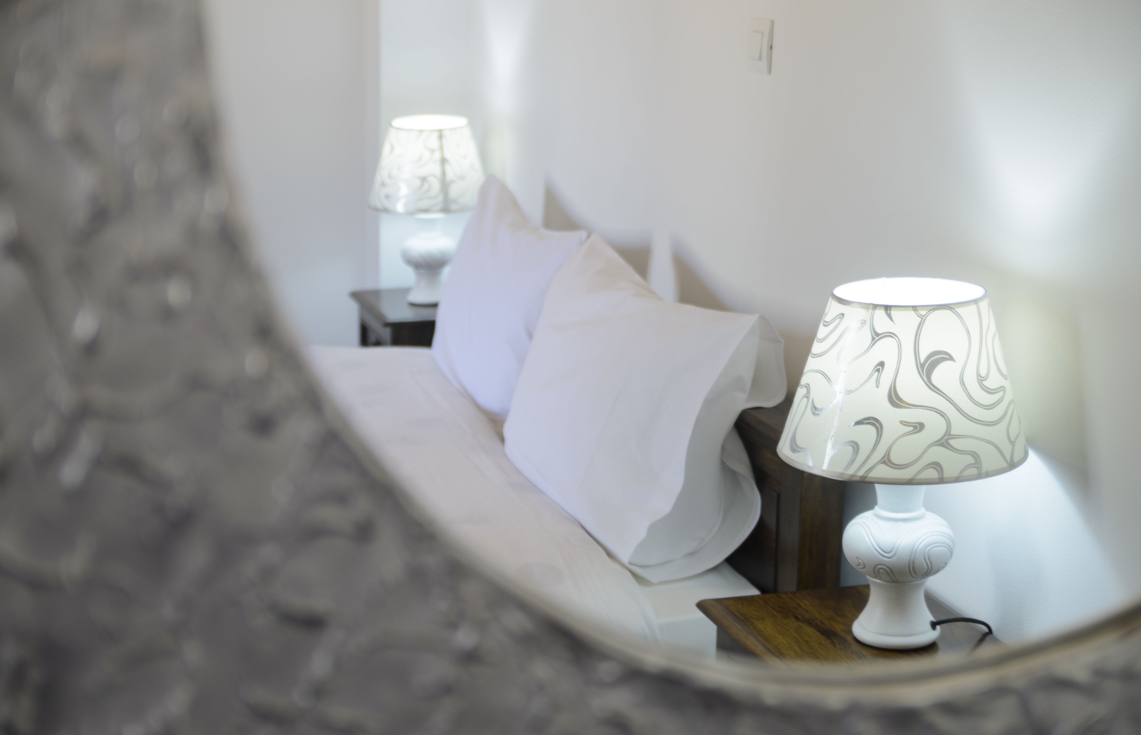 Una habitación de hotel con una cama, almohadas blancas y una lámpara con pantalla estampada.