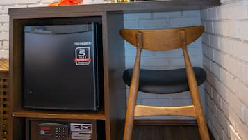 A compact kitchen with a refrigerator, a wooden chair, a hanging coat rack, and a potted plant.
