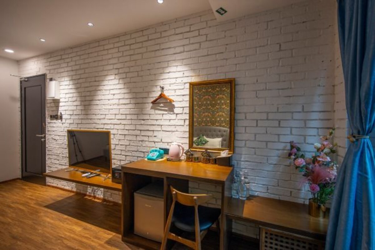 A room with a brick wall, a desk with a chair, a mirror, a hanging light, and a door.