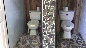 A bathroom with two toilets, a stone mosaic wall, and a patterned floor. - Costa Rica Glamping (La Virgen)