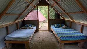 A small, enclosed room with two beds, a wooden bench, and a door leading outside. - Costa Rica Glamping (La Virgen)