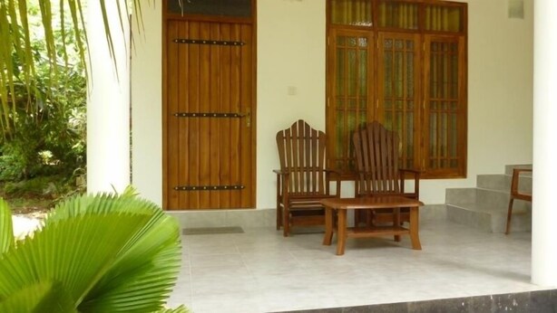 A covered porch with wooden furniture and a large window. - Serene Home Stay (Udawalawa)