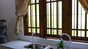 A kitchen with a sink, a water dispenser, and a window with bars. - Serene Home Stay (Udawalawa)