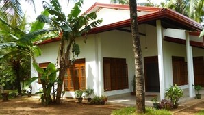 A white building with a red roof, surrounded by tropical plants and palm trees. - Serene Home Stay (Udawalawa)