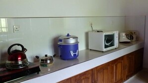 A kitchen with a kettle, a blue container, a microwave, and a toaster on the counter. - Serene Home Stay (Udawalawa)
