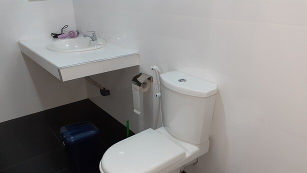 A bathroom with a white toilet, a sink, and a blue trash bin. - Serene Home Stay (Udawalawa)
