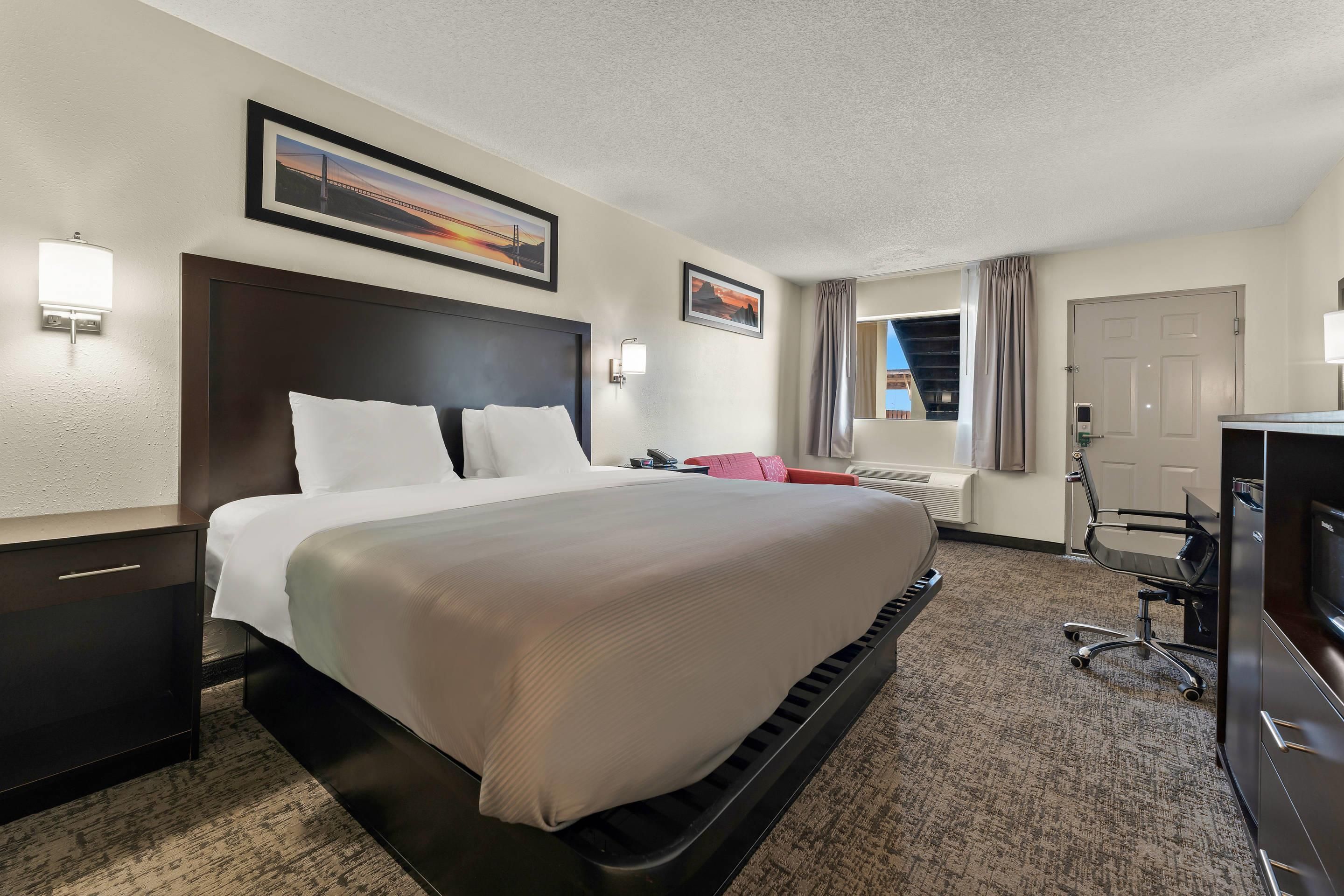 A hotel room with a large bed, a desk with a chair, a television, and a window with curtains.