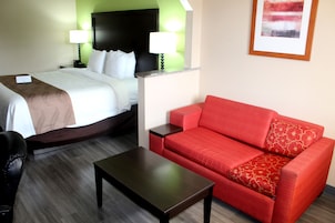 Una habitación de hotel con una cama, un sofá rojo, una mesita de café y dos lámparas de noche.