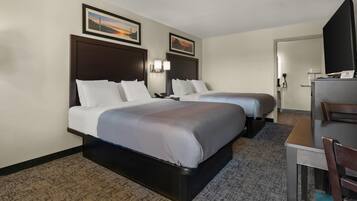A hotel room with two beds, a desk, a chair, a television, and a 'No Smoking' sign.