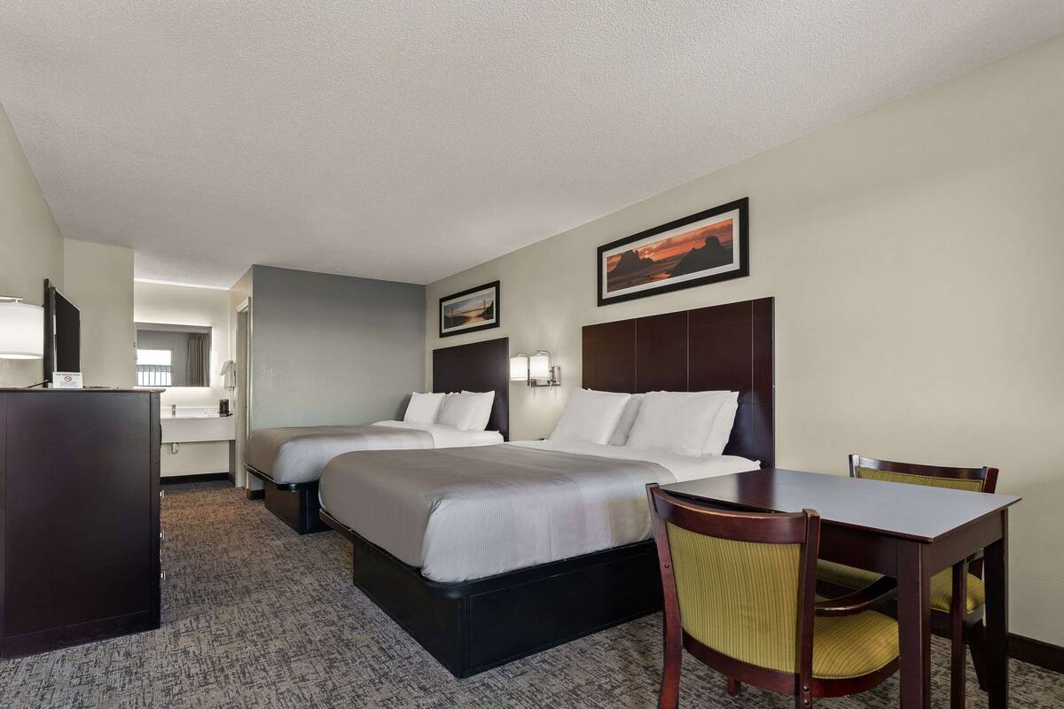 Habitación de hotel con dos camas, un escritorio y una silla. También hay un aparador y un espejo.