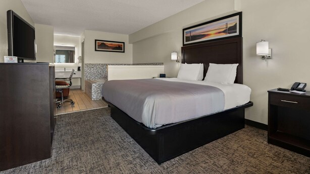 A hotel room with a large bed, a desk with a chair, a TV, and a painting on the wall. - Quality Inn & Suites Dublin (Dublin)