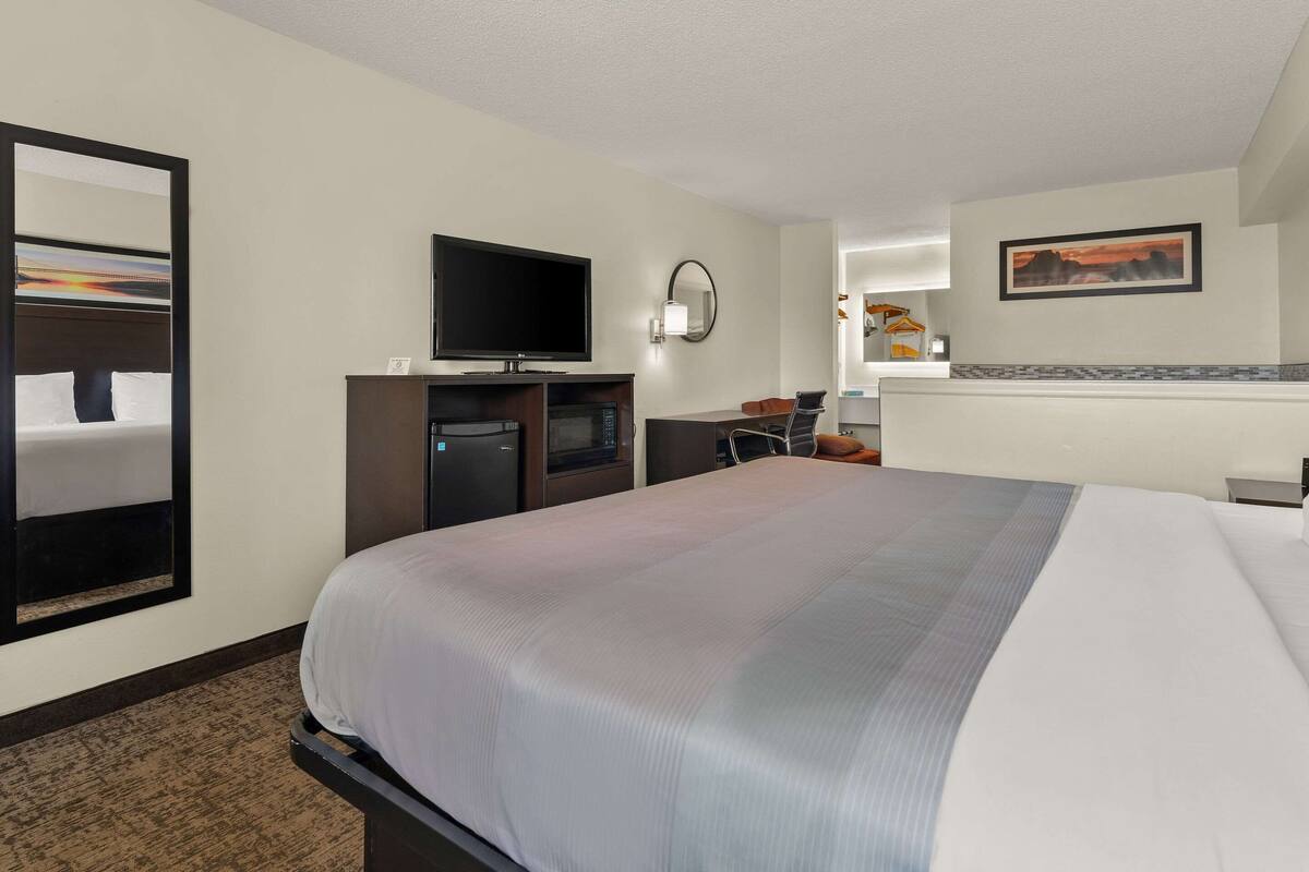 Una habitación de hotel con una cama grande, un televisor, un escritorio y un espejo.