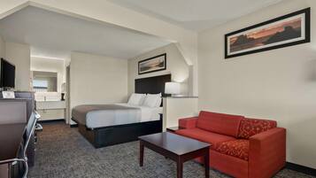 Quarto de hotel com cama, sofá vermelho, mesinha, televisão e um quadro na parede.