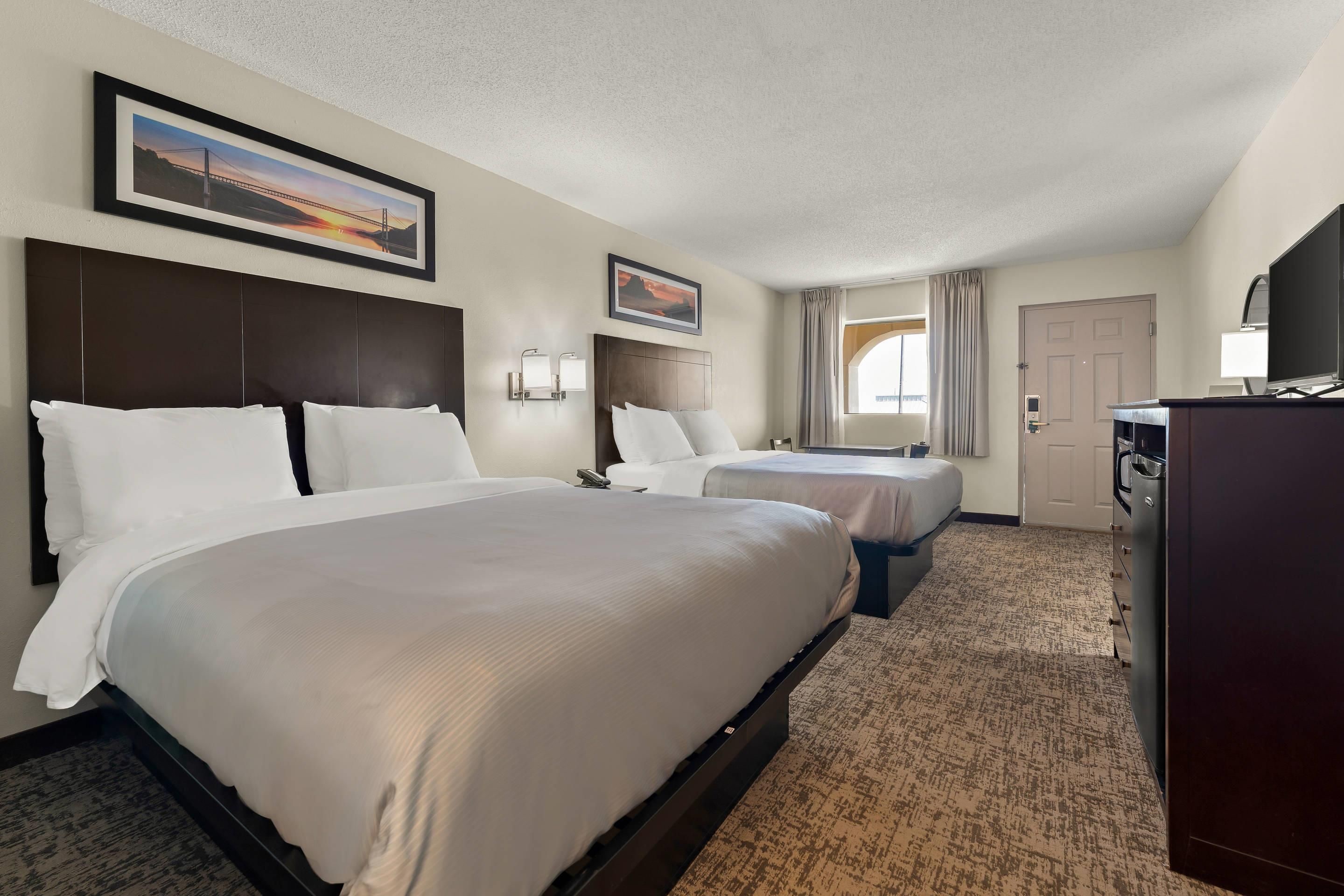 A hotel room with two beds, a desk, a television, and a door.