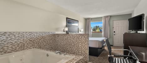 Habitación de hotel con una bañera grande, televisor, escritorio y una silla.