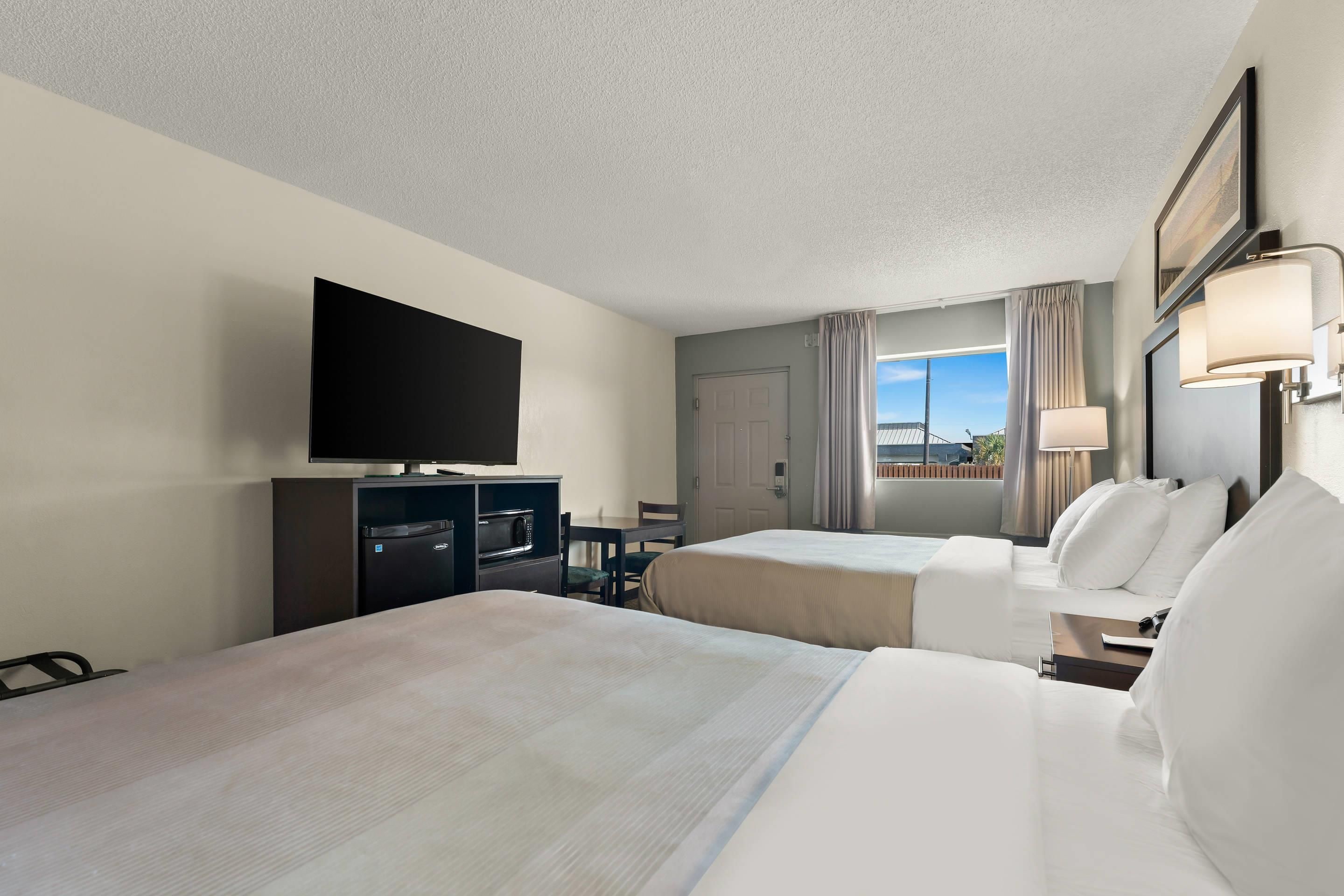 A hotel room with two beds, a television, a minibar, and a window with curtains.
