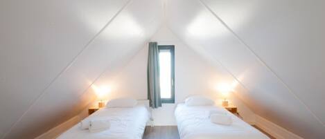 Une petite chambre mansardée, bien éclairée, avec deux lits simples, un plancher en bois et un puits de lumière.