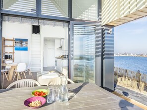 A modern kitchen with white cabinets, a dining area with a table set for two, and a view of the sea through large windows. - Oesterdam Resort by Interhome (Tholen)