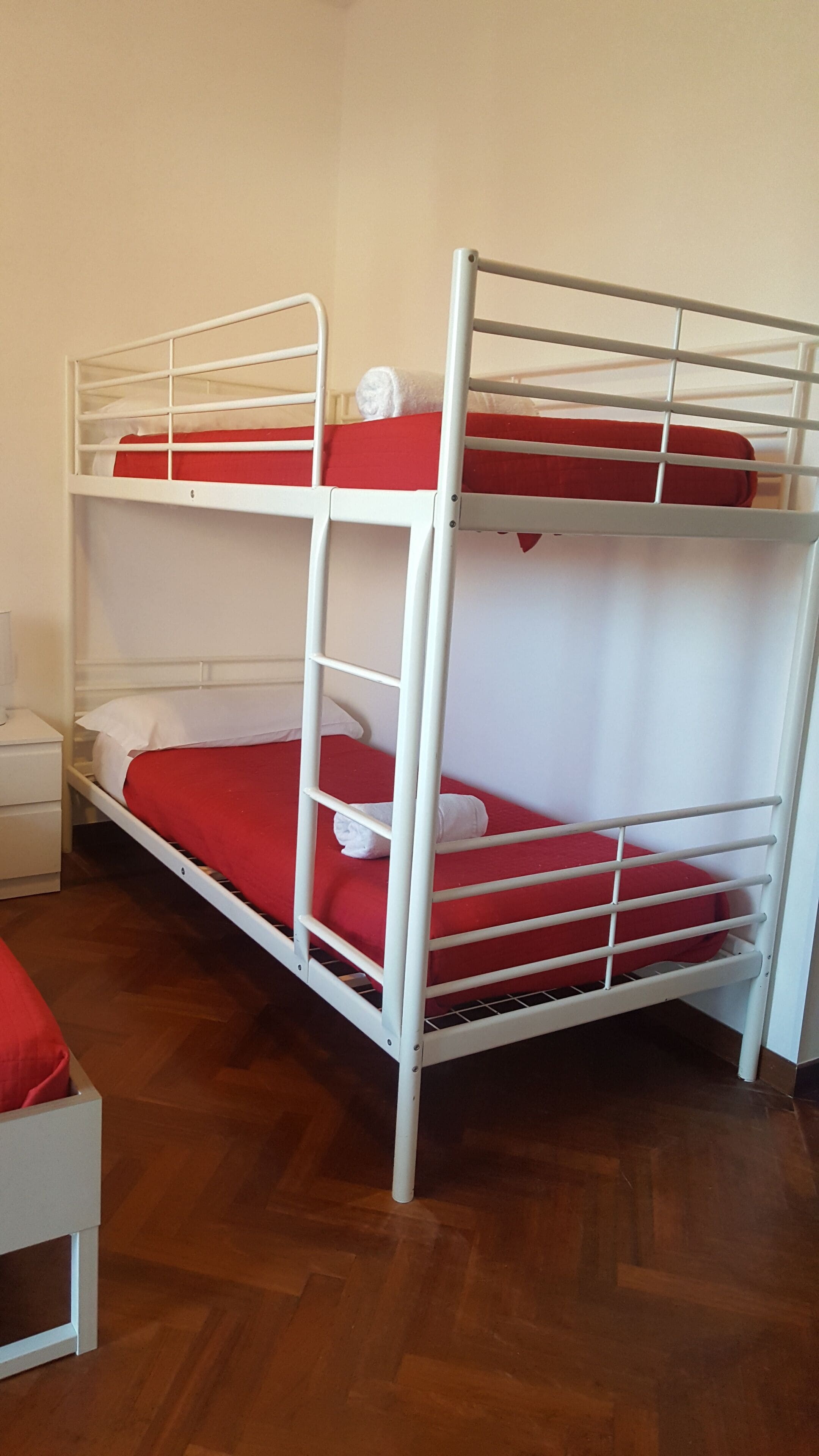 Una cama litera con ropa de cama roja en una habitación con suelo de madera y paredes blancas.