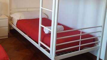Una cama litera con ropa de cama roja en una habitación con suelo de madera y paredes blancas.