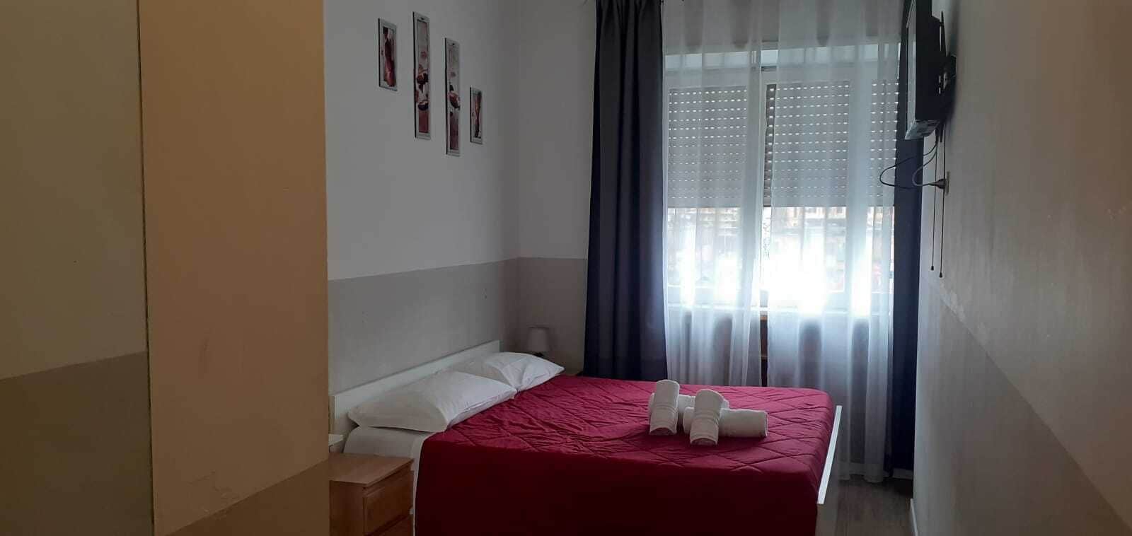 A bedroom with a bed, a nightstand, a wall-mounted TV, and a window with curtains.