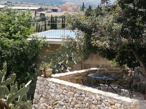 A stone wall with a table and chairs, surrounded by greenery and cacti. - Poggio del Gallo (Chiaramonte Gulfi)