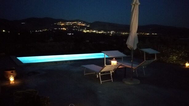 A rooftop terrace with a long, illuminated bench, a table, and a chair, along with a lantern and umbrella. - Poggio del Gallo (Chiaramonte Gulfi)