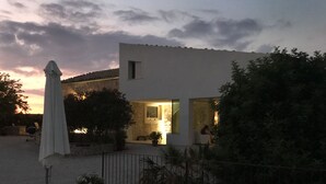 A modern building with a flat roof, a small window, and a door. There is a white umbrella and a potted plant in front of the building. - Poggio del Gallo (Chiaramonte Gulfi)