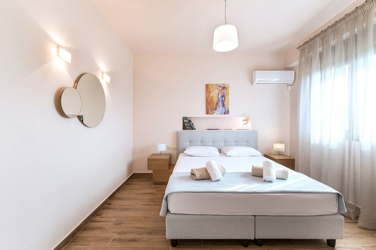 Quarto moderno com uma cama grande, mesas de cabeceira, espelho fixado na parede e ar condicionado.