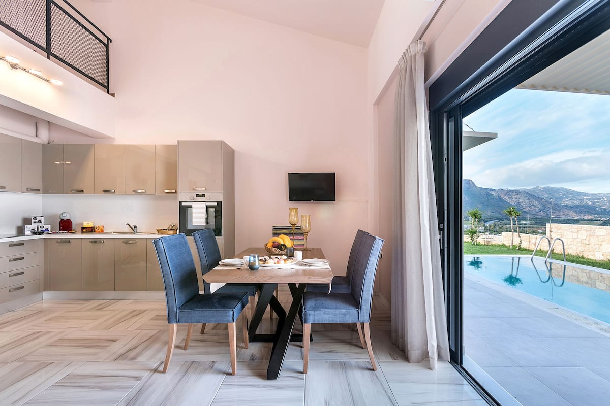 Cozinha moderna com área de refeições, TV e vista para piscina.