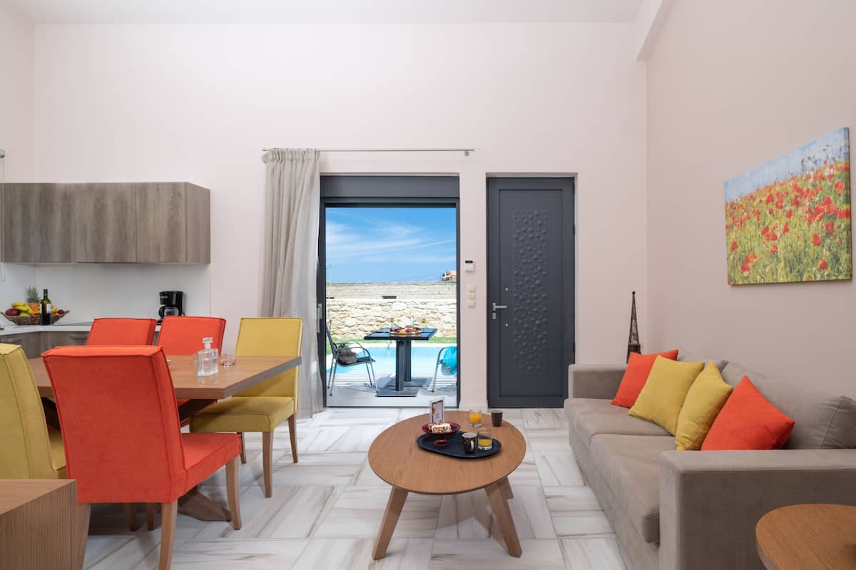 Uma sala de estar moderna com área de jantar, um conjunto de sofá e vista para a praia através de uma porta aberta.