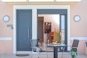 A dining area with a table set for two, chairs, and a view into a room with a painting.