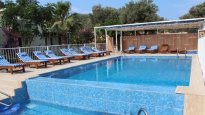 Una piscina con mosaicos azules, sillas de descanso y una valla de madera.