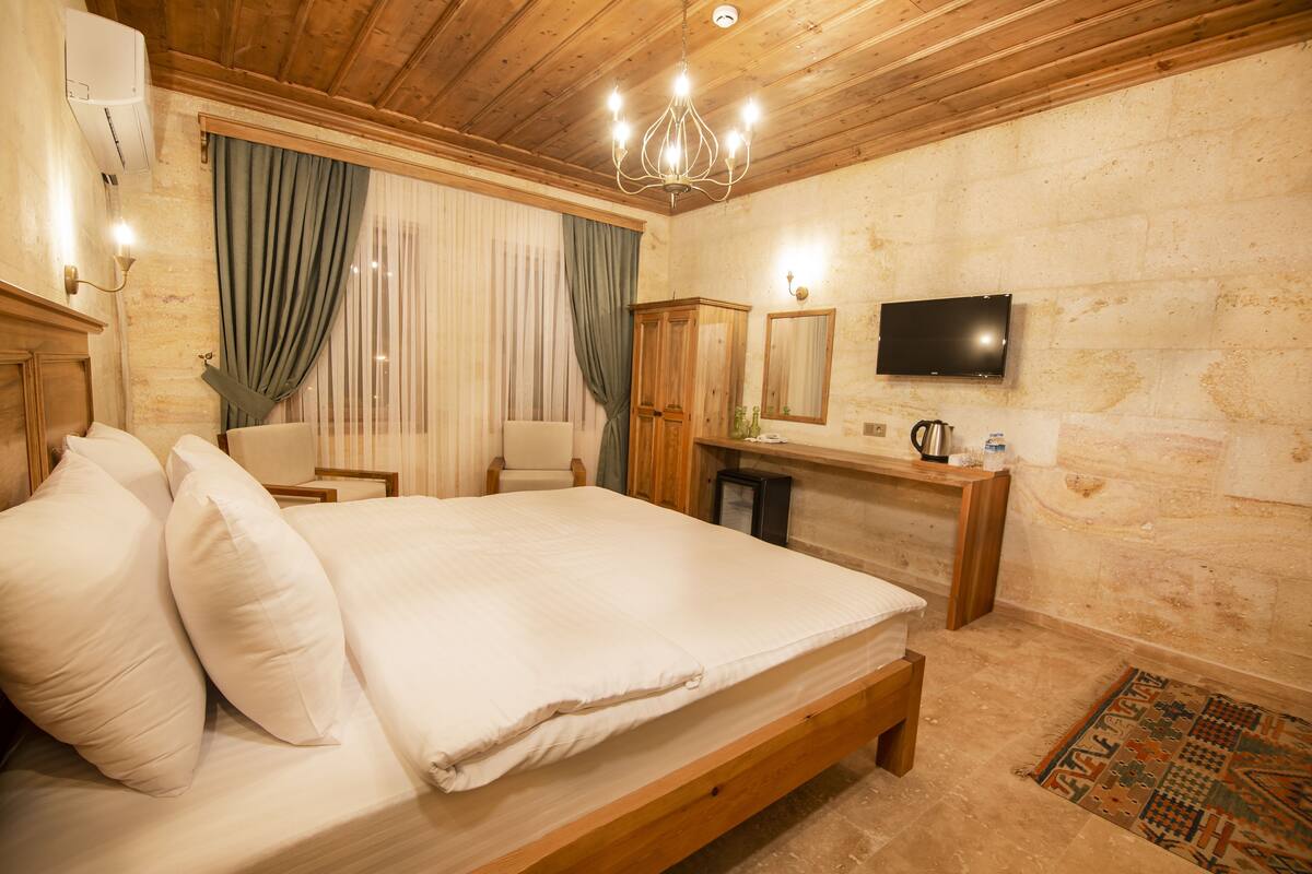 A bedroom with a wooden bed, a television, a mirror, a small table, and a window with curtains.