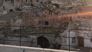A historic rock formation with multiple cave dwellings and a flag on top. - Ikarus Cappadocia Hotel (Nevsehir)