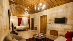 A room with a bed, a sofa, a table, and a TV mounted on the wall. - Ikarus Cappadocia Hotel (Nevsehir)