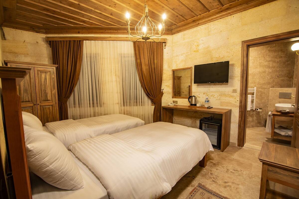 A room with two beds, a desk with a computer, a television, and a bathroom with a sink and mirror.