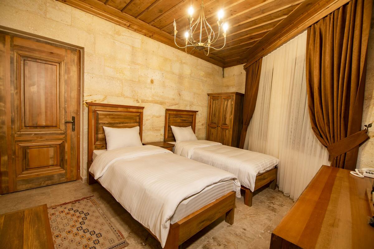 A room with two wooden beds, a chandelier, a wooden desk, and a telephone.